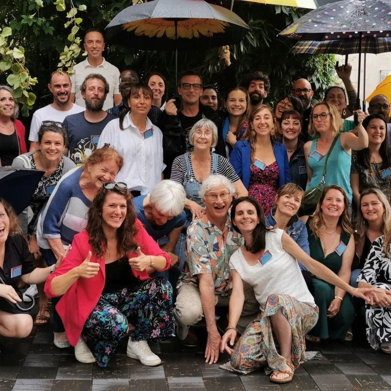 Grand groupe d'adultes souriants avec des parapluies colorés, réunis dans un jardin pour un anniversaire festif