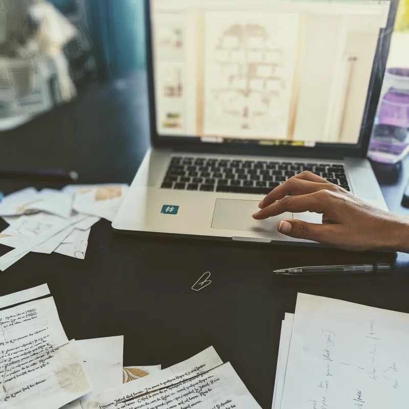 Table d'escape game : un plan affiché sur un ordinateur, une main qui cherche, indices et documents manuscrits étalés autour