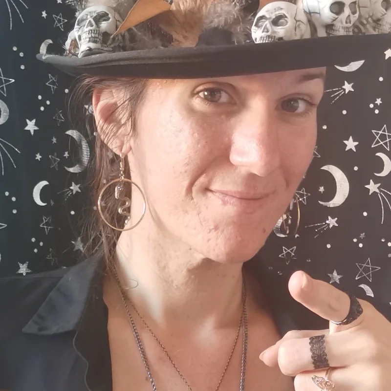 Claire Lys costumée en sorcière, haut-de-forme orné de crânes et de plumes, devant une tenture étoilée d'inspiration Halloween